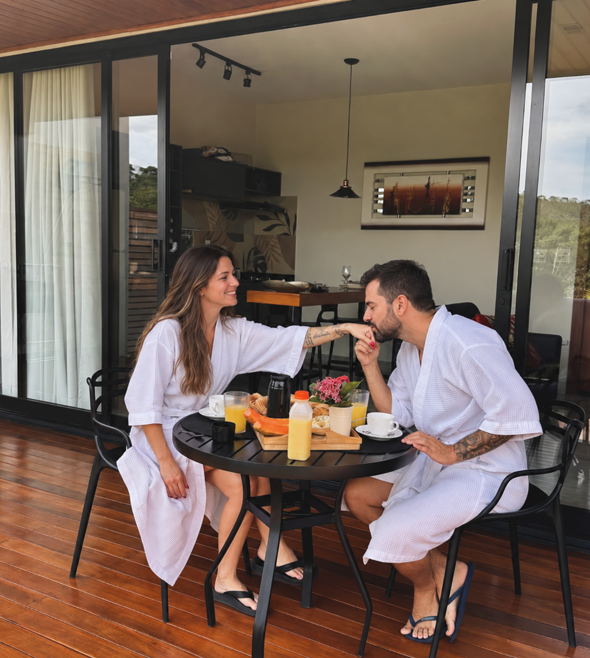 Casal de roupão tomando café da manhã na mesa externa do loft